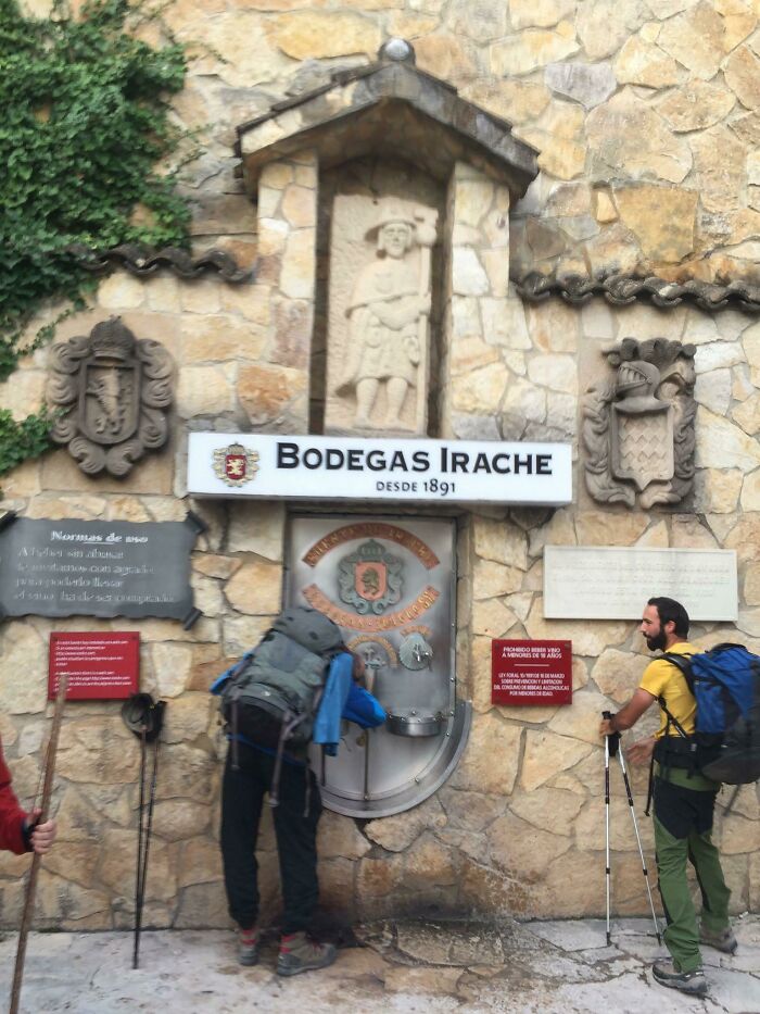 Personas con mochilas en Bodegas Irache sorbiendo vino de una fuente, una de las cosas que sorprendieron a los viajeros.