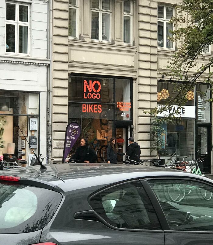 Tienda de alquiler de bicicletas sin logo en ciudad europea con viajeros sorprendidos por lo diferente en otros países.
