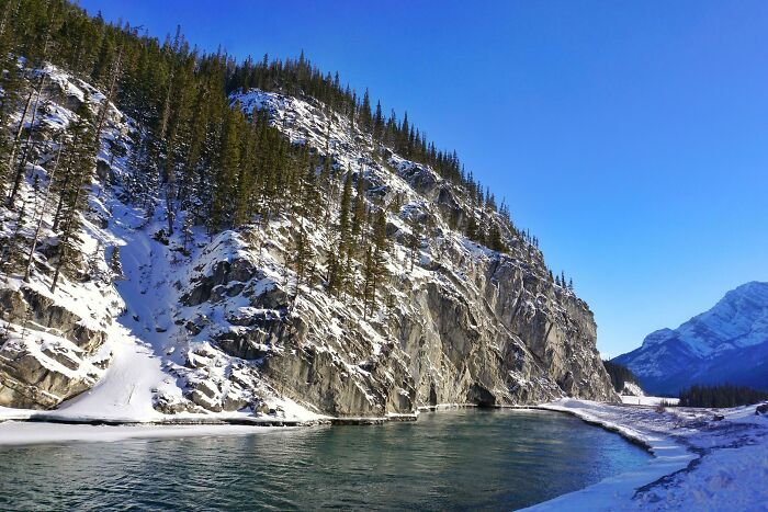 Paisaje de Canadá con río, nieve y montañas al fondo bajo un cielo despejado.