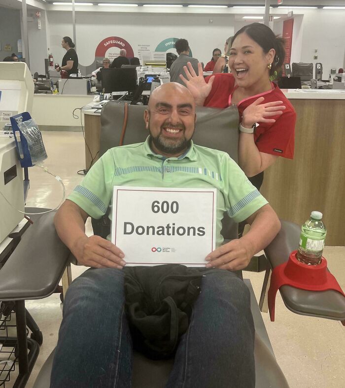 Hombre sonriente en Canadá sosteniendo un cartel de 600 donaciones, acompañado por una mujer en un centro de donación.
