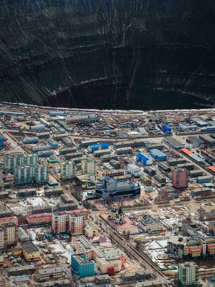 Vista aérea de una ciudad cerca de un enorme cráter, reflejando el «infierno urbano» creado por humanos.