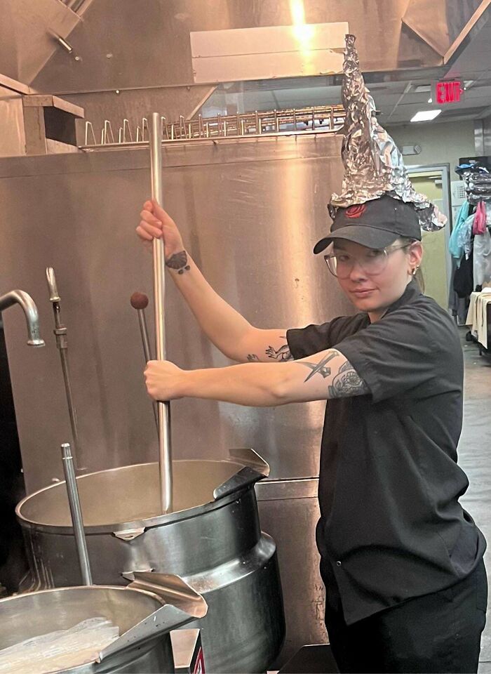 Empleado de hostelería con gorro de aluminio revolviendo una gran olla en la cocina.
