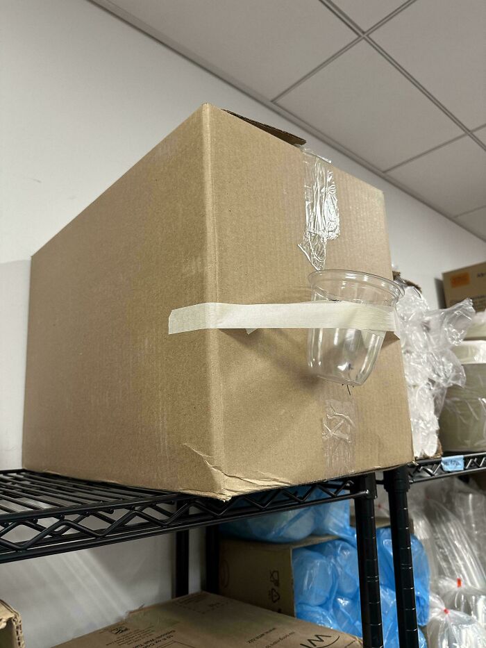 Caja en un estante con un vaso de plástico mal pegado, mostrando frustraciones comunes en hostelería.