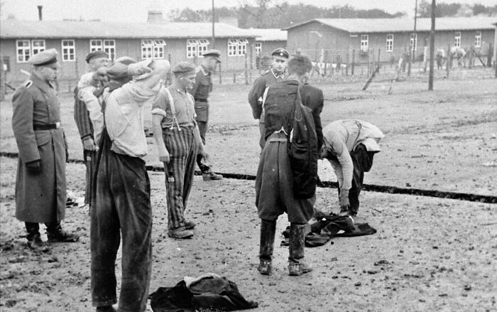 Prisioneros en un campo de concentración vigilados por soldados durante la Segunda Guerra Mundial, mostrando escenas históricas impactantes.