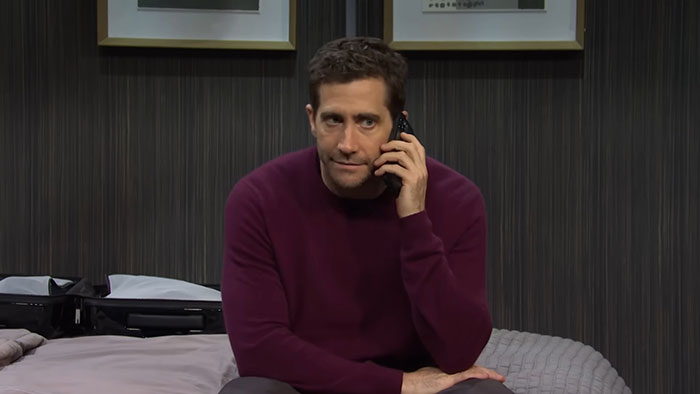 Un actor en una habitación oscura hablando por teléfono, con un gesto serio, ejemplificando mal comportamiento.