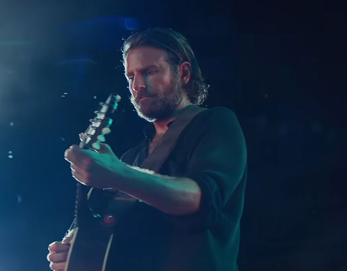 Hombre tocando guitarra en escenario con luces suaves, relacionado con historias de actores y opiniones cambiantes.