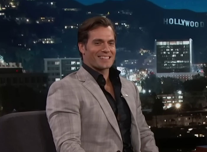 Actor en traje gris frente al letrero de Hollywood, relacionado con historias de mal comportamiento.