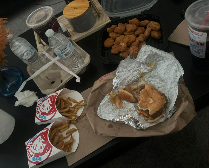Comida rápida sobre una mesa, incluyendo hamburguesa, papas fritas y nuggets, simbolizando comportamientos típicos de hombres.