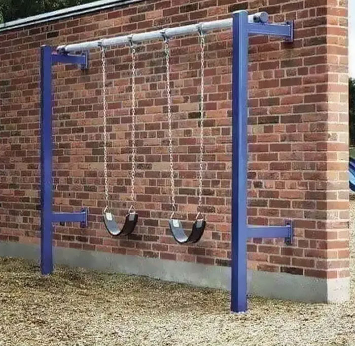 Columpios instalados frente a una pared de ladrillos, muestra un fallo arquitectónico gracioso.