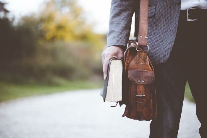 Hombre con libro y bolso de cuero, representando reflexiones sobre estupideces dichas con seriedad en entorno natural.