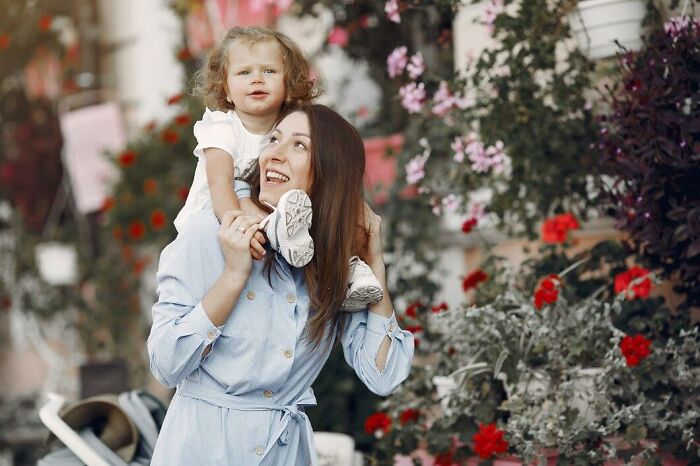 Mujer sonriente cargando niña sobre sus hombros en jardín con flores, ilustrando momentos de estupideces dichas con seriedad.
