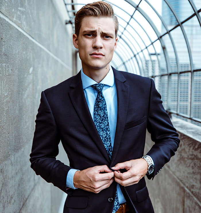 Hombre en traje elegante, ajustando su chaqueta, en una escena urbana; tema de apariencia sexy en libros vs. vida real.