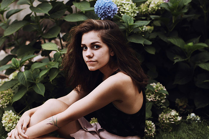 Joven sentada en un jardín, rodeada de hortensias, reflexionando sobre contrastes entre libros y vida real.
