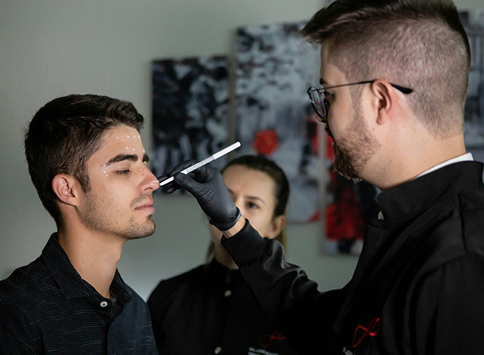 Man undergoing plastic surgery consultation, marking areas on his face with a professional.
