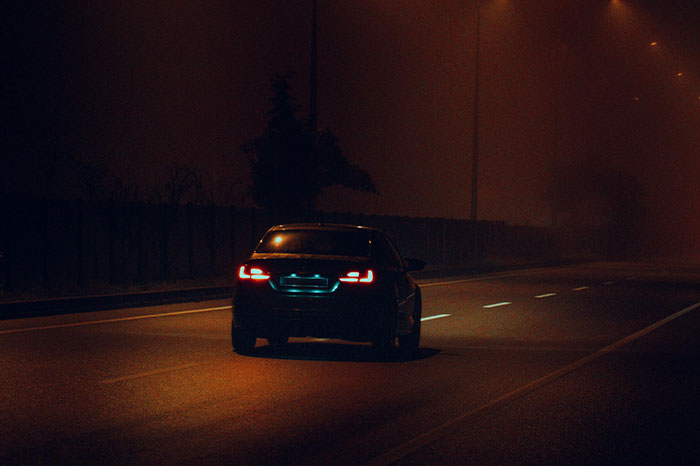 Coche conduciendo de noche en una carretera desierta, simbolizando la necesidad de irse ya mismo.