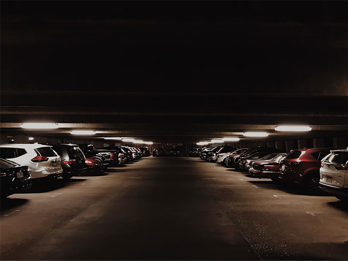 Estacionamiento oscuro con coches estacionados, creando una atmósfera que indica la necesidad de irse ya mismo.