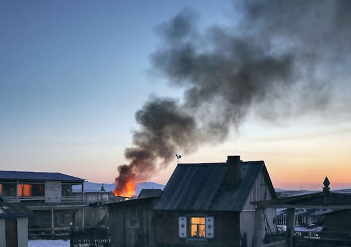 Casa en fuego en un vecindario al atardecer, humo denso elevándose, mostrando un momento para irse ya mismo.