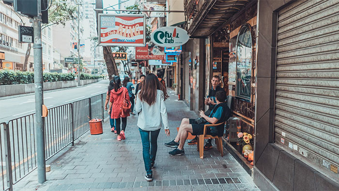 Personas caminando por una calle concurrida con tiendas, destacando la necesidad de irse ya mismo.