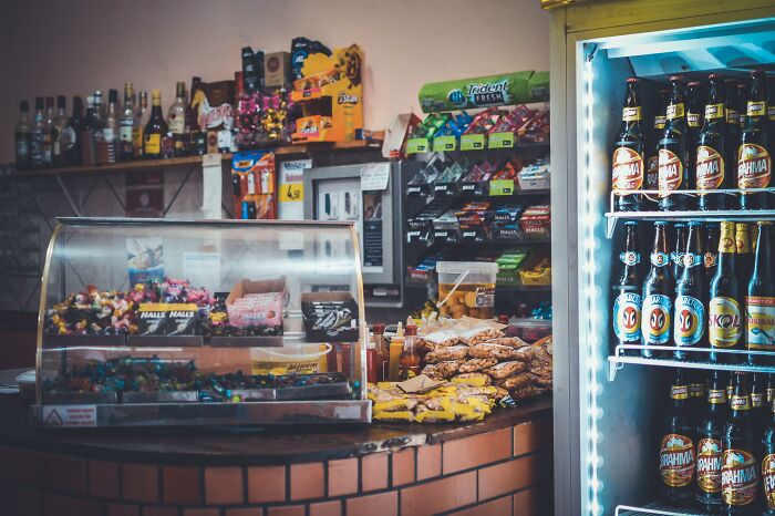 Tienda con dulces, refrigerador y botellas, lugar de conversaciones escuchadas accidentalmente.