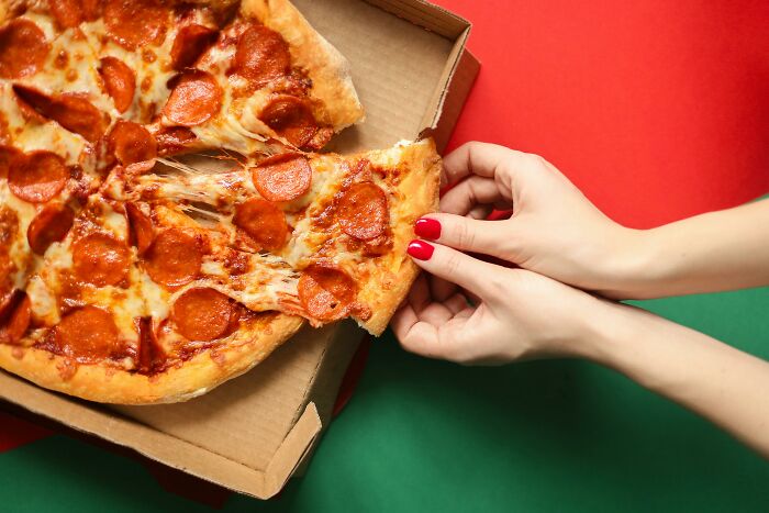 Manos sacando una porción de pizza de pepperoni de la caja. Conversaciones interesantes y deliciosas.