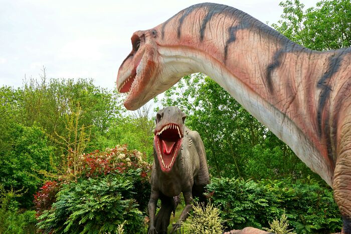 Dos dinosaurios animatrónicos en un parque temático rodeados de vegetación.