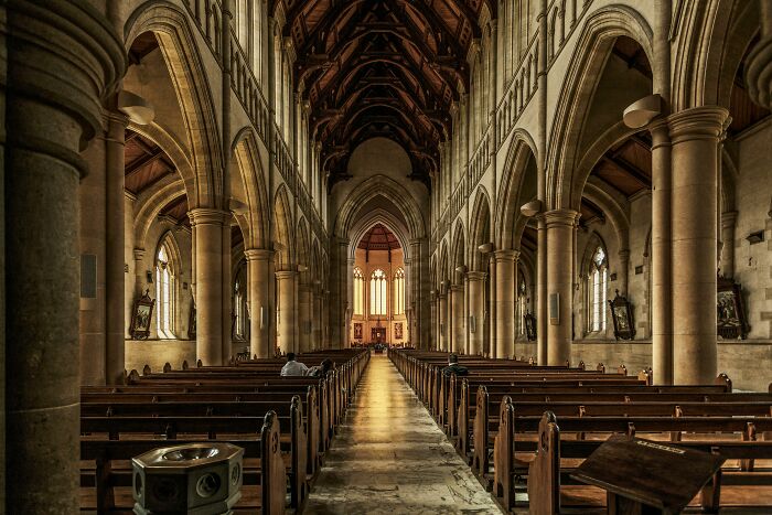 Interior de una iglesia gótica con bancos y columnas, luz natural iluminando las detalles arquitectónicos.