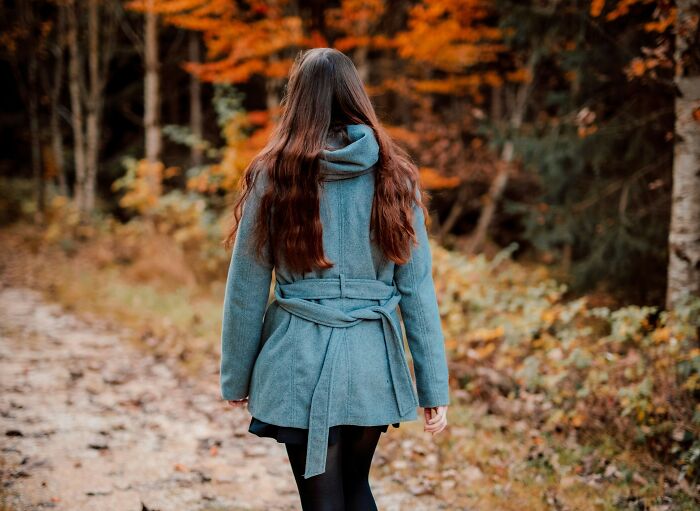 Persona caminando por un sendero en el bosque durante el otoño, con un abrigo azul.