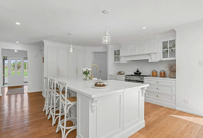 Cocina moderna con isla blanca, taburetes altos y suelo de madera, mostrando tendencias de interiorismo poco prácticas.