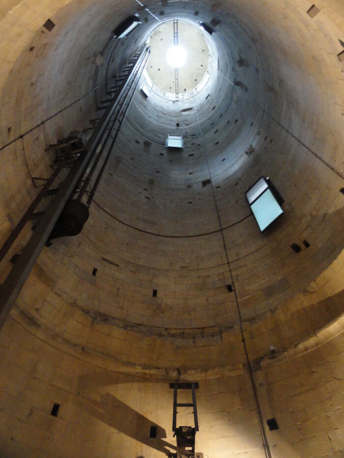 Perspectiva única desde el interior de una estructura cilíndrica, mostrando escaleras y luz natural al fondo.