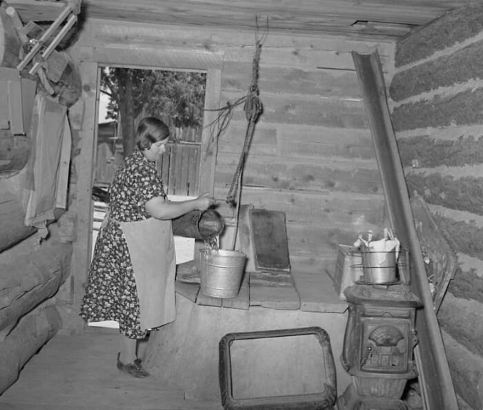 Mujer en cocina antigua vertiendo agua en un balde, recordando los días pasados en un entorno histórico.