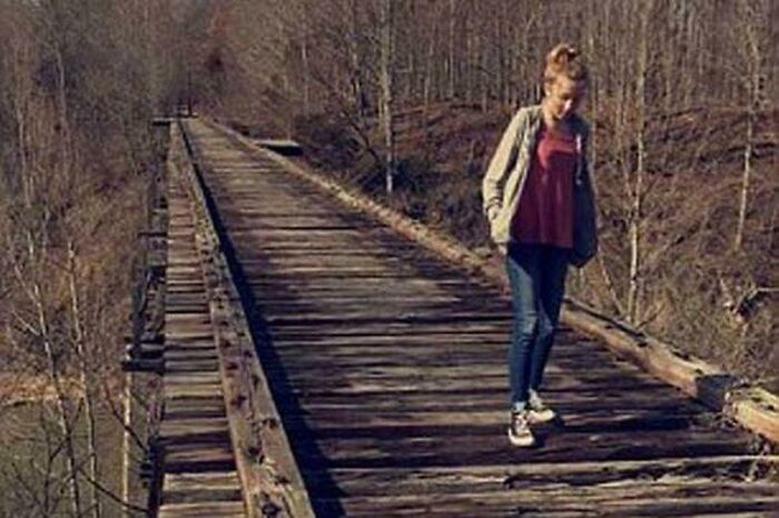 Una chica camina por un antiguo puente de tren en el bosque, todo parece normal.