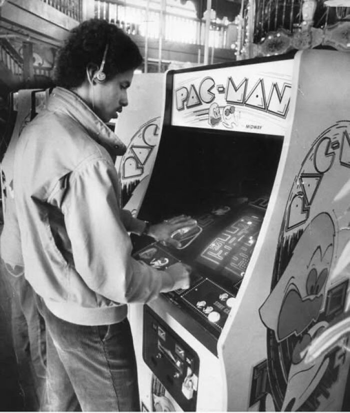 Hombre jugando en una máquina arcade de Pac-Man, recordando días pasados en un entorno de videojuegos retro.