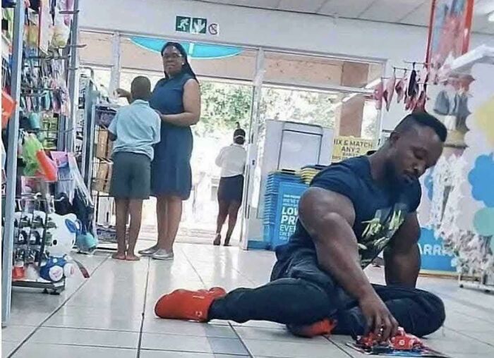 Hombre musculoso juega en el suelo de una tienda; escena rara y curiosa en un entorno cotidiano.