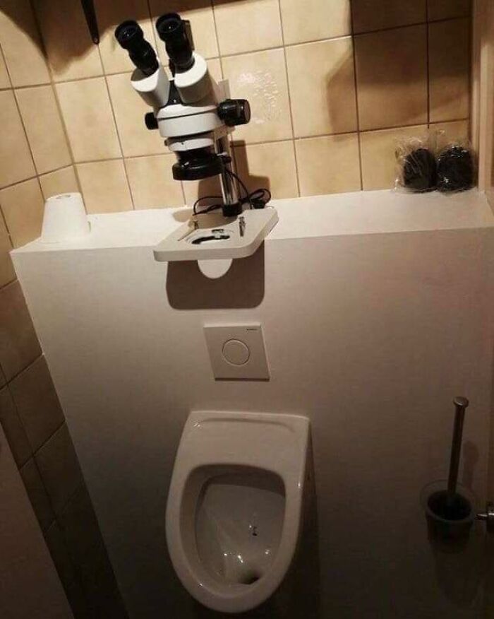 Microscopio instalado encima de un urinario en un baño, creando una imagen rara y absurda.