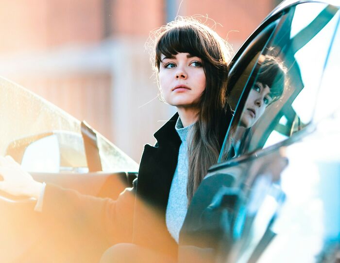 Mujer joven sentada en un auto, con abrigo negro, reflejada en el vidrio. Datos útiles para situaciones imprevistas.