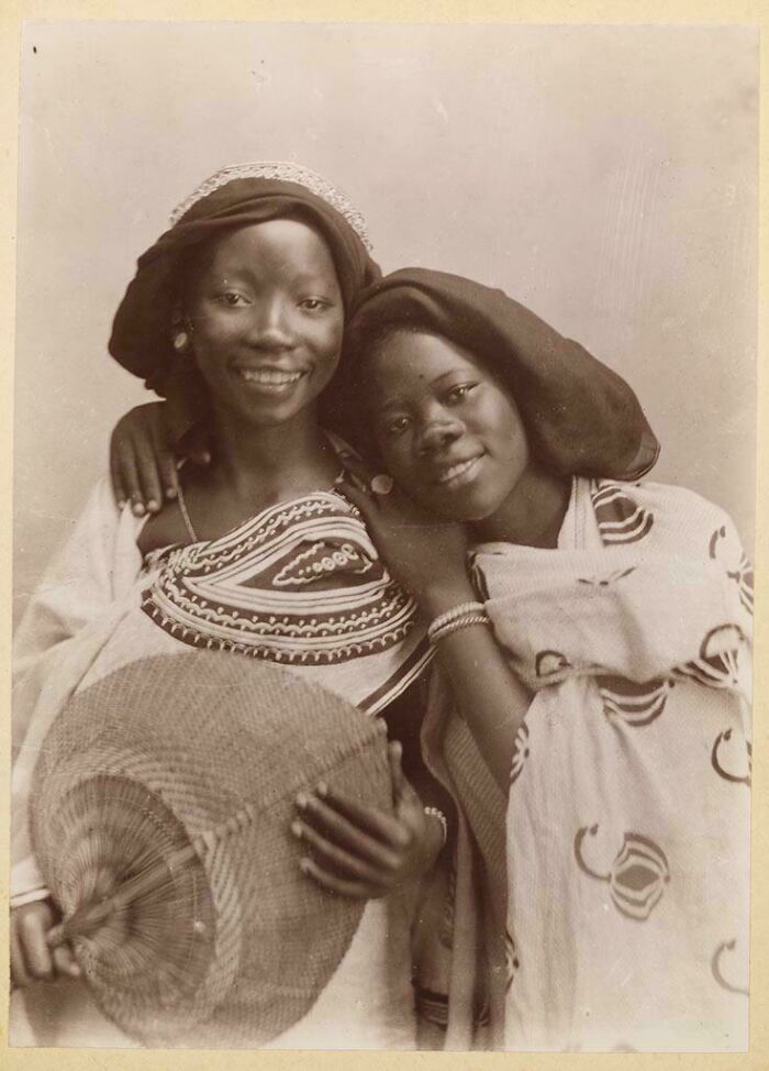 Dos mujeres africanas sonriendo vestidas con ropa tradicional en una foto histórica fascinante en blanco y negro.
