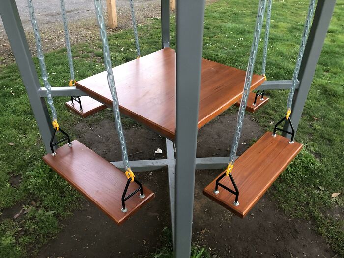 Diseño curioso de columpios y mesa en un parque, que no parece práctico en la realidad.