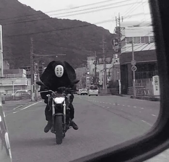 Persona con máscara montando motocicleta en una escena absurda y rara en la carretera.
