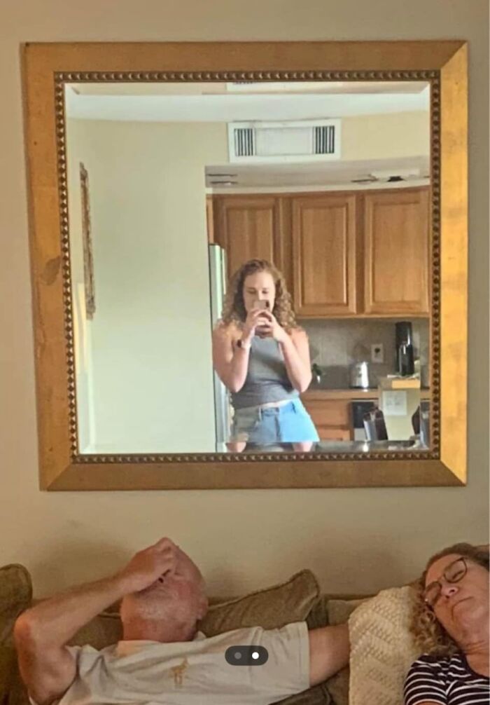 Mujer tomando selfie en espejo, con personas descansando en el sofá, mostrando la venta de cosas raras.