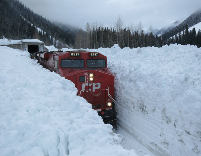Tren canadiense avanzando por túnel de nieve profunda en un paisaje invernal.
