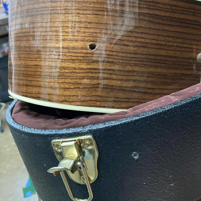 Estuche dañado con agujero, guardando guitarra de madera, resaltando accidentes costosos.