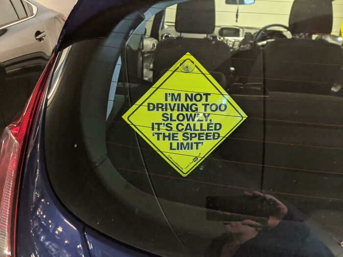 Coche con cartel pasivo-agresivo sobre límite de velocidad en la ventana trasera.