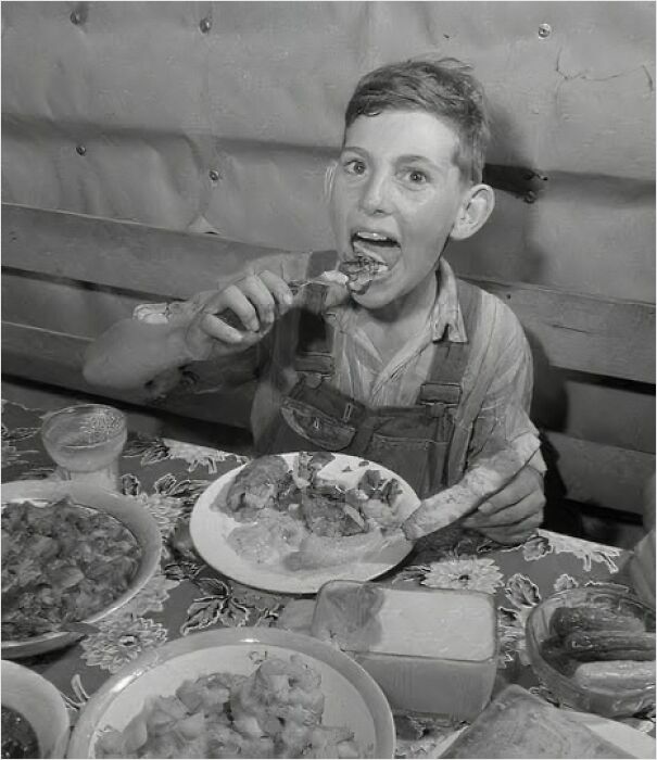 Niño comiendo pollo en una mesa con comida, reflejando momentos históricos pasados.