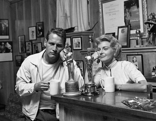 Pareja disfrutando de café junto a trofeos en una sala con fotos históricas.