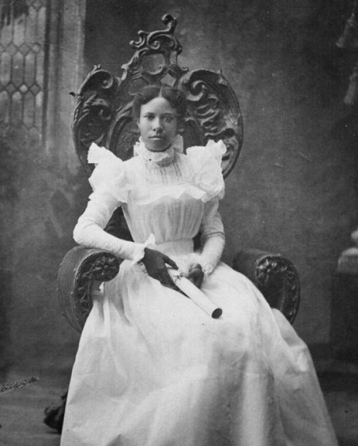 Mujer en vestido blanco de época sentada en silla tallada sosteniendo un pergamino en fotos históricas fascinantes.
