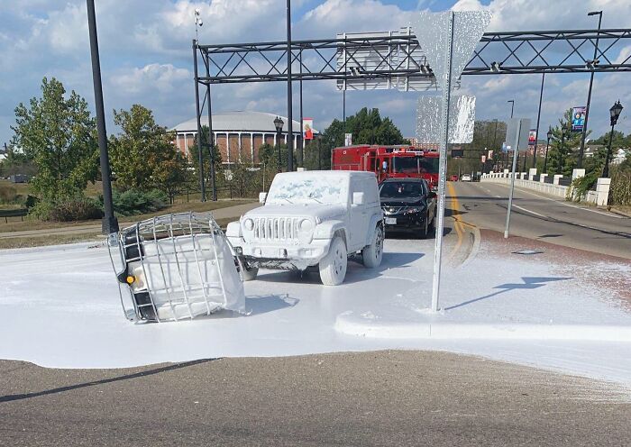Jeep cubierto de pintura blanca tras un accidente en la carretera, con un camión de bomberos en el fondo.
