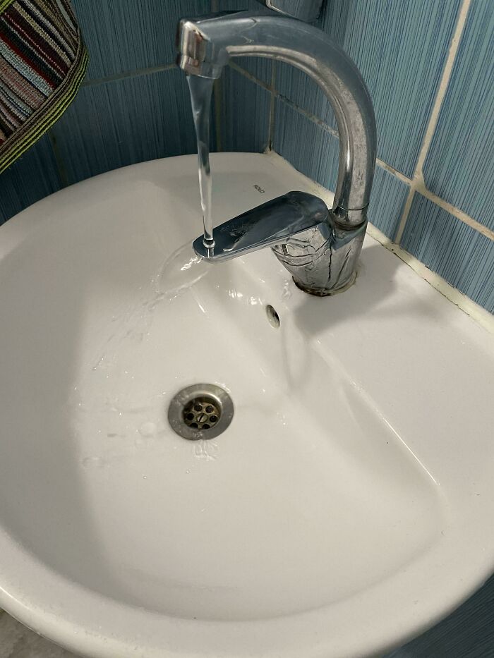 Grifo mal diseñado con agua fuera del lavabo, mostrando un ejemplo de diseño que no funciona en la realidad.