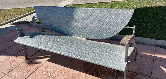 Banco de metal con diseño inusual al sol, un ejemplo de diseño en papel que no funciona en la realidad.