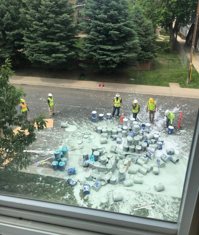 Trabajadores de obra observan un accidente caro: derrame de pintura en la calle.