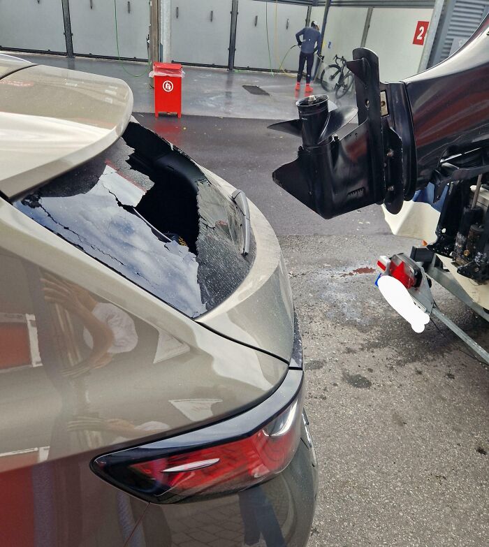 Coche dañado por accidente caro en estacionamiento, con motor de barco incrustado en la ventana trasera.